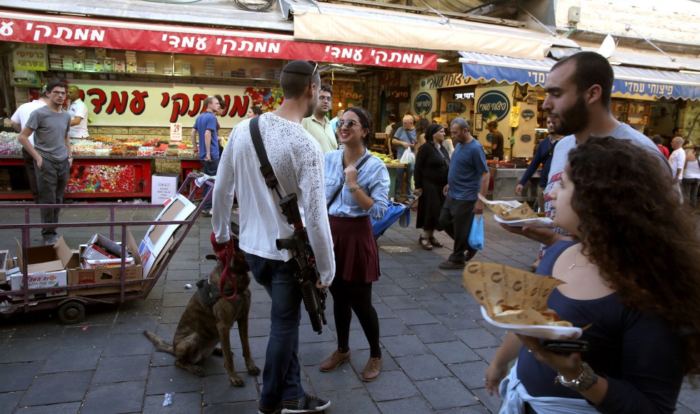 Young Israelis (mostly soldiers on weekend vacation) carry their personal rifles at the Jerusalem outdoors Mahne Yehuda market on October 9, 2015. The mayor of Jerusalem, Nir Barkat, has gone as far as to encourage residents who own guns to carry them around with them "Possessing weapons increases the confidence of residents," he said as he toured occupied and annexed east Jerusalem, with his own gun in full sight. AFP PHOTO / GALI TIBBON / AFP PHOTO / GALI TIBBON